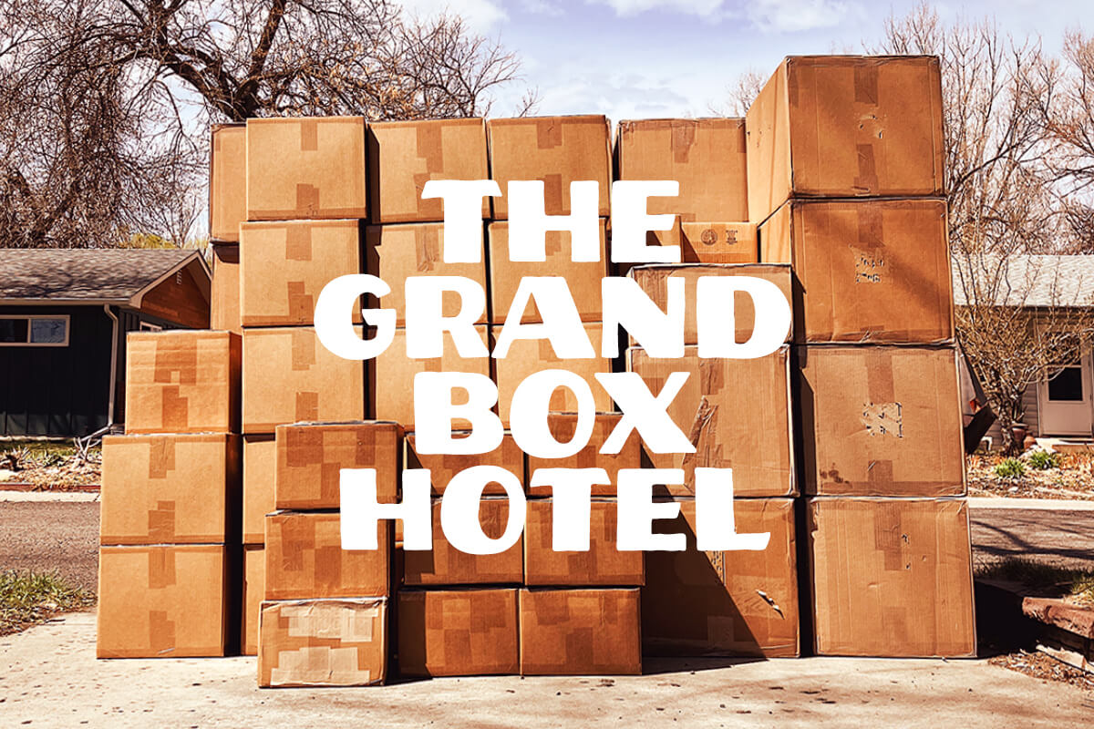 Stack of boxes in a driveway with The Grand Box Hotel title in Wes Anderson Grand Budapest Hotel style